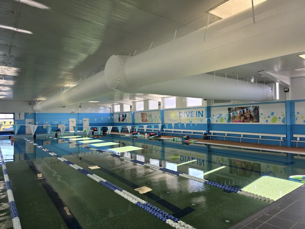 Indoor 25 m pool hall with a white fabric supply-air duct running the length of the ceiling