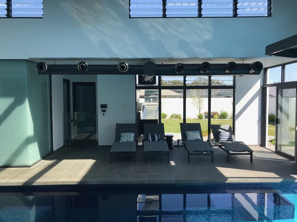 Indoor pool room with a row of black jet diffusers supplying conditioned air above the water