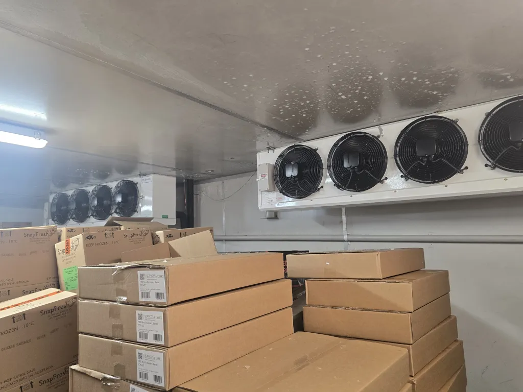 Ceiling-mounted evaporator fan units in a cold storage room stacked with cartons