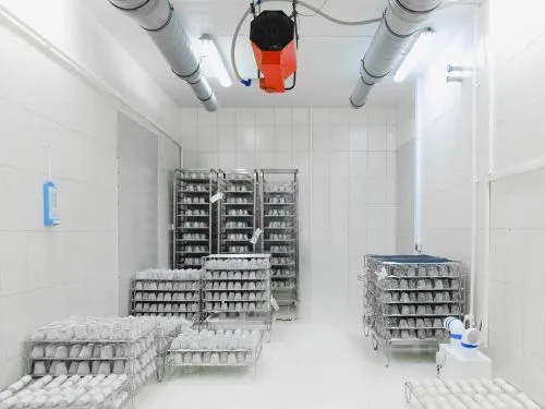 Tiled food processing room with racks of product trays and a ceiling-mounted air unit
