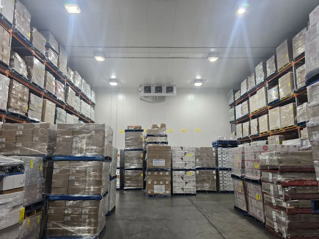 Storage room stacked with palletised cartons under a ceiling-mounted cooling unit